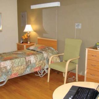 A hospital room with a bed, chair, lamp, and dresser.