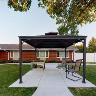 A backyard with a gazebo, chairs, and a patio in front of a house.