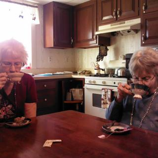 Two elderly women enjoying tea in a cozy kitchen setting.