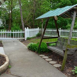 A peaceful garden scene with a wooden swing and a white picket fence.