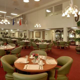 An elegant restaurant interior with neatly arranged tables and chairs, featuring classic lighting fixtures and a carpeted floor.