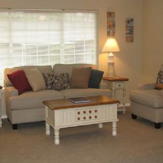 A cozy living room with a sofa, armchair, coffee table, and a lamp by the window.