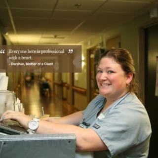 A nurse smiling while working on a computer in a hospital hallway.