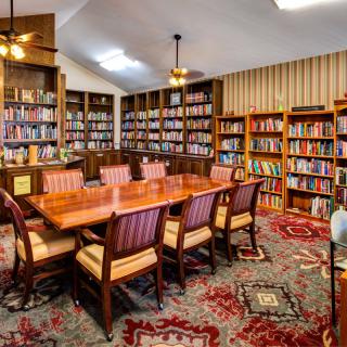A cozy library room with wooden furniture and shelves filled with books.
