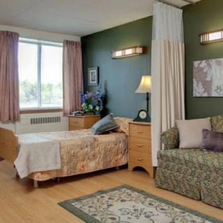 A cozy hospital room with a bed and a sofa, featuring warm lighting and a window with curtains.