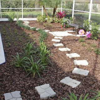 A garden with a curvy pathway made of stepping stones surrounded by mulch and greenery.