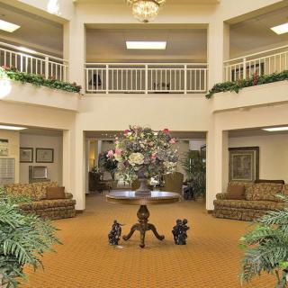 A spacious lobby with elegant decor, featuring comfortable seating, greenery, and a central chandelier.