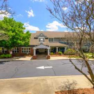 A two-story building with an entrance surrounded by trees and a driveway under a blue sky.