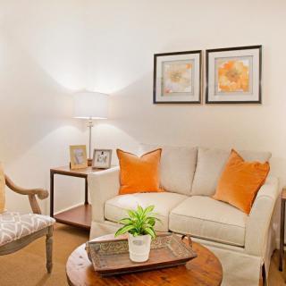 A cozy living room featuring a cream sofa with orange pillows, complemented by a side table, lamp, and wall art.
