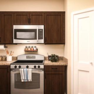 A modern kitchen with brown cabinets, featuring a stainless steel stove and microwave.