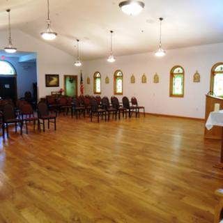 An empty chapel room with wooden floors and rows of chairs.