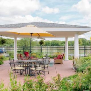 A tranquil outdoor patio area featuring a table with chairs and a large umbrella under a gazebo in a garden setting.