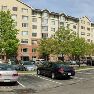 A view of an apartment building with a parking lot surrounded by trees.