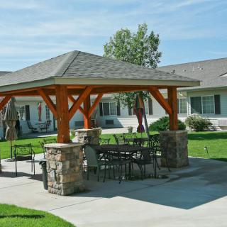 A wooden gazebo with outdoor seating on a lawn patio.