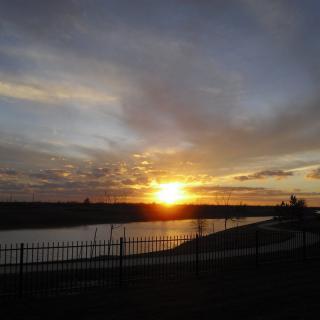 A serene sunset over a river with a silhouetted fence in the foreground.