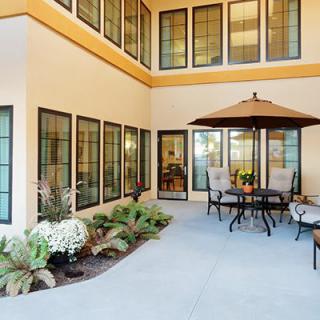 A cozy patio area with outdoor furniture and an umbrella, surrounded by large windows and decorative plants.