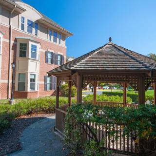 A peaceful outdoor scene with a gazebo beside a brick building under a clear blue sky.