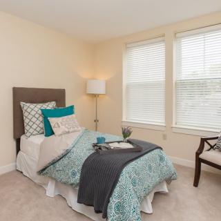 A cozy bedroom with a single bed, decorative pillows, and a floor lamp by the window.