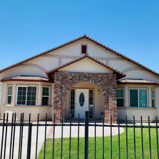 A residential house with a brick entrance and fenced front yard under a clear blue sky.