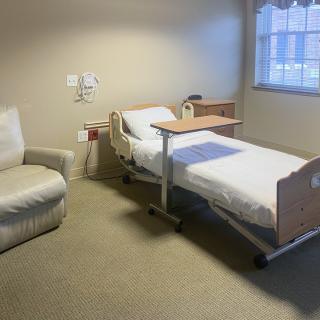 An empty hospital room with a single bed and a chair by the window.