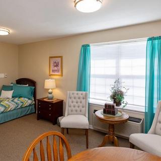 A cozy bedroom with a bed, chairs, and a window with blue curtains.