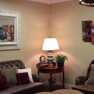 A cozy living room with a leather sofa, decorative pillows, framed artwork on the walls, and a warm table lamp illuminating the space.