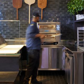 A chef is preparing food in a modern restaurant kitchen with a pizza oven.