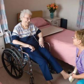 Elderly woman in a wheelchair receiving assistance from a caregiver in a nursing home.