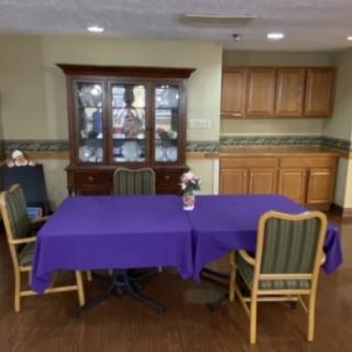 A dining area with a purple tablecloth-covered table and chairs set against a cabinet backdrop.
