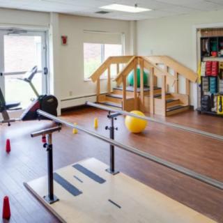 A physical therapy room equipped with parallel bars, a stationary bike, and an exercise ball for rehabilitation exercises.