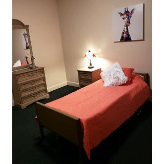 A cozy bedroom with a single bed and orange bedding, featuring a dresser and wall art.
