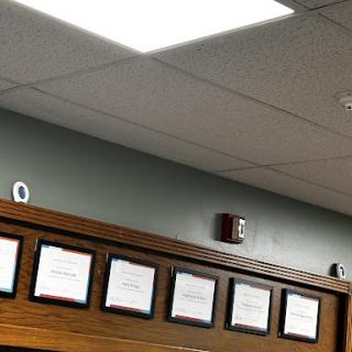 A view of a well-organized office wall displaying several certificates beneath bright ceiling lights.