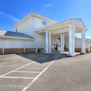 A white building with a columned entrance and adjacent parking area under a clear blue sky.