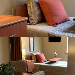 A cozy bedroom with a single bed adorned with pillows, a nightstand, and a small lamp by the window.