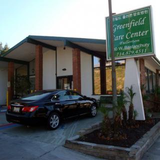 A clinic entrance with a car parked in the driveway and a sign displaying the name of the facility.