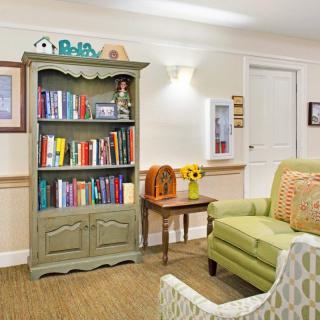 A cozy living room featuring a green bookshelf filled with colorful books, a light green sofa, and a small wooden table with decorative items.
