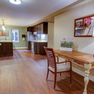 A modern kitchen and living space with wooden flooring, featuring a small desk and chair in the foreground.