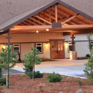 A welcoming entrance to a building with wooden architectural elements, surrounded by neatly arranged landscaping in the evening.