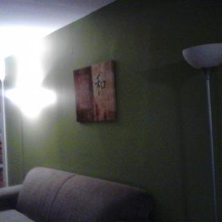 A cozy living room with a sofa against a green wall, featuring a floor lamp and wall art.