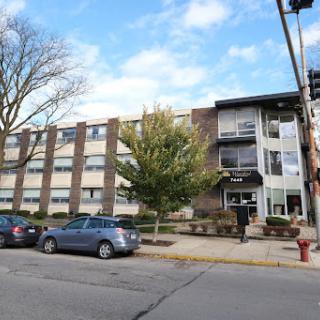 A view of a multi-story building surrounded by trees and parked cars on the street.