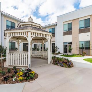 A charming courtyard featuring a wooden gazebo and well-maintained landscaping in front of a modern building.