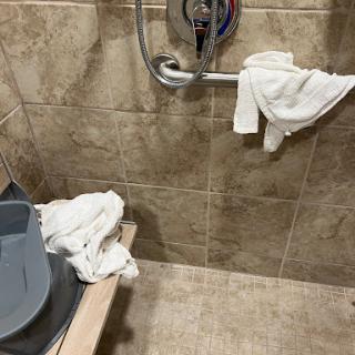 A corner of a bathroom shower area featuring towels and cleaning supplies.