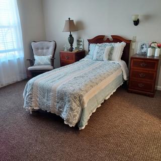 A cozy bedroom with a single bed, comfortable chair, and wooden furniture.