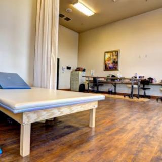 A spacious therapy room with a treatment table and office desk.