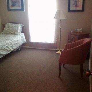 A cozy bedroom with a bed, chair, and a standing lamp positioned by the window.
