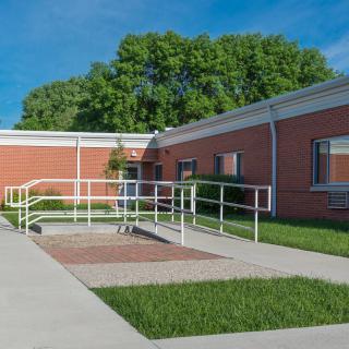 A brick building with an accessibility ramp and surrounding greenery.