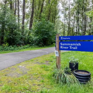 Entrance to the Sammamish River Trail surrounded by lush greenery and trees.