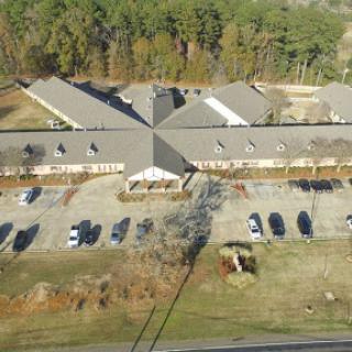 An aerial view of a residential building complex surrounded by trees and a parking area.
