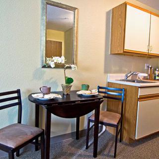 A compact kitchen and dining area with a small table and chairs, featuring a mirror and a simple setup.