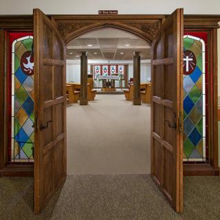 An interior view of a chapel with wooden doors and colorful stained glass panels.